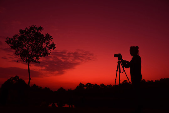 Photographer taking pictures outdoors, silhouette of a woman with camera over sunset