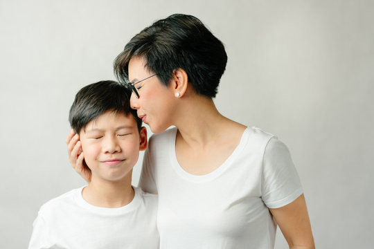 A smart and beautiful Asian mom hold and kiss her preteen son. The boy leans to his mother smile, feel happy and grateful. Love expression, Parenting teen, Single mom, Young son, Mommy's love Concept.