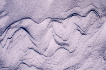 The surface of the snow cover in the light of the sun, with abstract patterns formed by the wind, a copy space, close-up, toned.