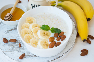 The concept of proper nutrition. Healthy Breakfast of oatmeal with banana and nuts in a white plate on a white background. Horizontal orientation. Close up