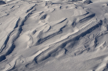 Fototapeta premium The surface of the snow cover in the light of the sun, with abstract patterns formed by the wind, a copy space, close-up.