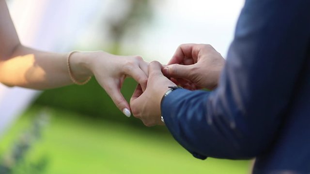 Man wear ring for the lady, groom and bride hands while wearing in wedding ceremony on blur grass field on background