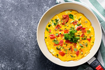 scrambled eggs with tomatoes, spinach and pumpkin seeds in frying pan on black background