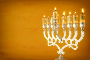 Religion image of jewish holiday Hanukkah background with menorah (traditional candelabra) and oil candles over yellow background