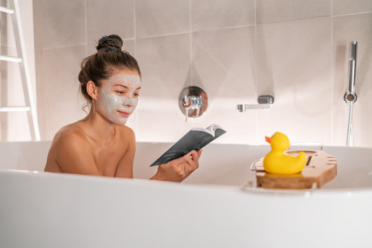 Bath at home woman relaxing taking a warm bath reading book cozy enjoying free time putting facial clay mask pampering weekend. Bubble bath spa time.