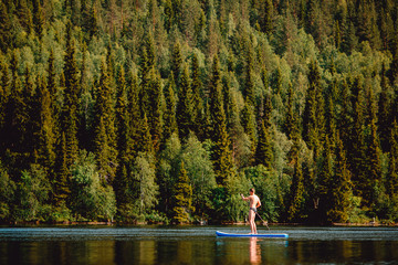 Fototapeta na wymiar Man rowing oar on sup board blue lake water paddleboard background of forest