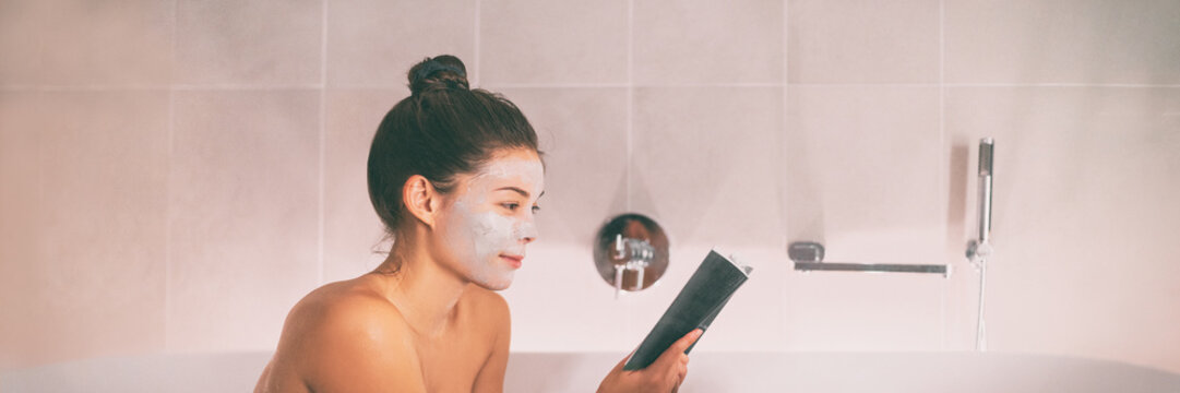 Woman putting face mask clay product reading a book relaxing in hot bath on unwind spa pampering weekend in luxury resort banner panorama. Asian girl taking a bath in bathtub.