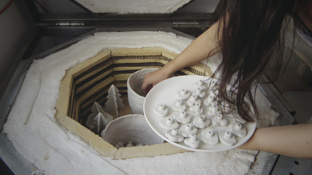 Closeup of asian female master potter puts small raw clay products into a kiln for firing. Professional potter works in workshop