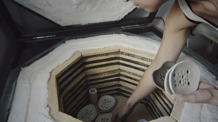 Asian female potter puts raw clayware and soap dishes made of clay into a kiln for firing