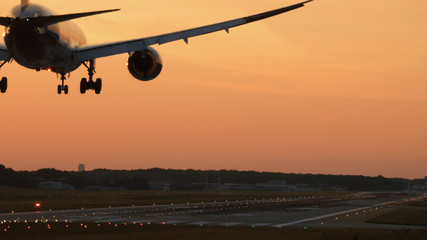 Rear view of widebody twin engine airplane landing in the early morning. Picturesque sunset at the background,