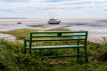 A bench with a view towards two boats in the low tide and the Ormonde Wind Farm in the background, seen in Haverigg, Cumbria, England, UK