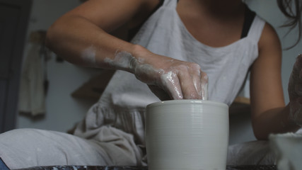 Fototapeta na wymiar Master female potter molding wet clay into a bowl with wet sponge on potter's wheel. Female potter works in studio.