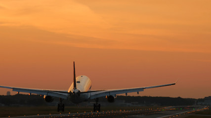 Rear view of twin engine widebody airplane land on at the dawn. Moment of touch the runway.