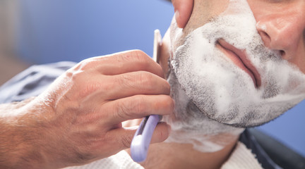 Obraz na płótnie Canvas Hands of barber holding razor and shaving a client.
