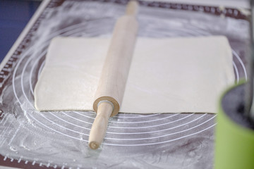 A sheet of rolled puff pastry and a wooden rolling pin on a silicone dough Mat. The cooking process of baking. Homemade cake.