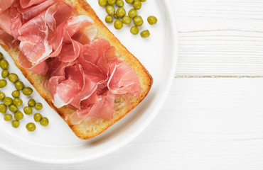 bruschetta or open sandwich with Italian ham and green pea in white plate. white wood background