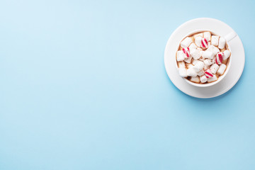 Cup of hot chocolate with marshmallow cocoa powder and caramel on pastel blue background with copy space. Christmas winter concept.