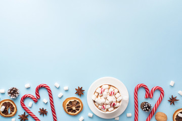 Cup of hot chocolate with marshmallow cocoa powder and caramel nuts, oranges on pastel blue background with copy space. Christmas winter concept.