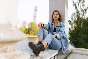 Portrait of a longing pensive teenage girl dressed in denim and boots, sitting outside looking at...