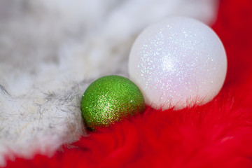 Green and white christmas ball on red and white fur. Balls shine in the light. Selective shallow focus on a green ball. Copy space.