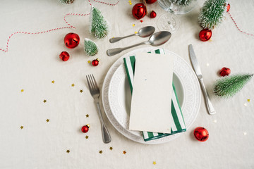 Fototapeta na wymiar Beautiful Christmas table setting with space for menu or invitation over white plates with silver cutlery, festive vintage decoration on linen tablecloth background. Holiday layout.