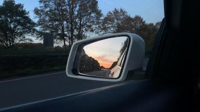 Colorful golden sunset view in car window mirror on highway,close up