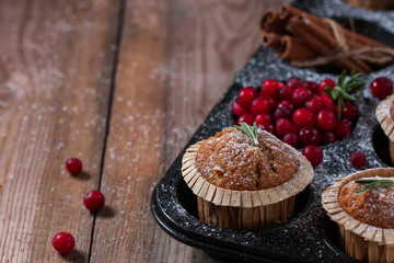 Fresh homemade Cranberry muffins in baking form on wooden table with Christmas decoration. Muffins in eco-friendly recyclable paper packaging. Selective focus, copy space.