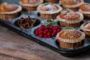 Fresh homemade Cranberry muffins in baking form on wooden table with Christmas decoration. Muffins in eco-friendly recyclable paper packaging. Selective focus, copy space.