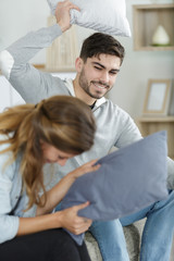 happy couple jokingly holds the pillow fight on the sofa