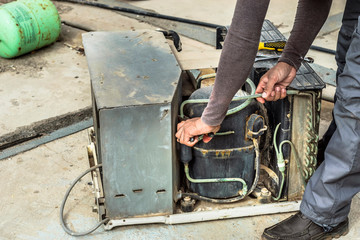 a professional electrician man is fixing the heavy unit of an air conditioner at the roof top of a building and wearing blue uniform and head cap