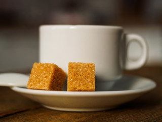 A white Cup of coffee and two cubes of yellow sugar