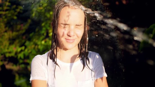 Slow motion video of splashing water from garden hose in teenage girls face at garden