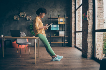 Full size profile side photo of cool smart afro american girl entrepreneur use tablet work read start-up news wear yellow shirt green pants trousers in office loft - Powered by Adobe