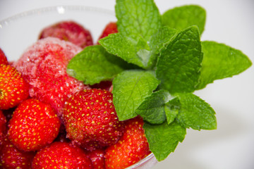 frozen strawberries with mint leaves in a glass on a white background