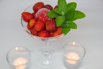 frozen strawberries with mint leaves in a glass and candles on a white background