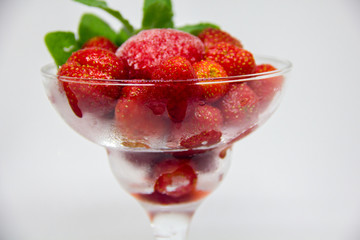 frozen strawberries with mint leaves in a glass on a white background