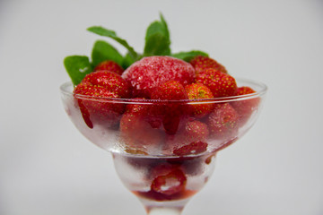 frozen strawberries with mint leaves in a glass on a white background