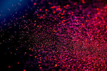 Red/purple shiny glitter on black background with blue light. Macro shot, shalow DOF.