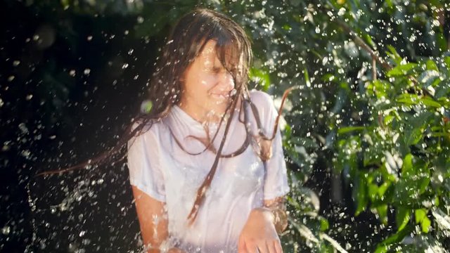 Closeup slow motion video of pouring water from bucket on smiling teenage girl in the garden at hot summer day
