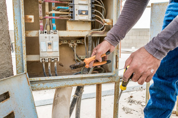 a professional electrician man is fixing the critical problems of electric supply of heavy duty air conditioner units on the roof top and wearing blue uniform & cap and the city is in the background 