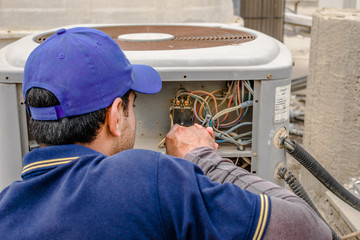 a professional electrician man is fixing the heavy unit of an air conditioner at the roof top of a building and wearing blue uniform and head cap