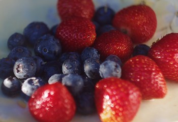 Blueberries and strawberries on ceramic plate. Wooden background. Fresh food vegan breakfast.