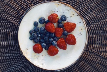 Blueberries and strawberries on ceramic plate. Wooden background. Fresh food vegan breakfast.