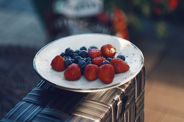 Blueberries and strawberries on ceramic plate. Wooden background. Fresh food vegan breakfast.