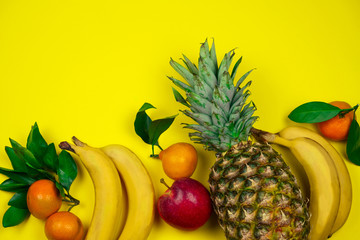 top view fresh tropical fruits layout pineapple,bananas, apple and tangerines on a yellow background