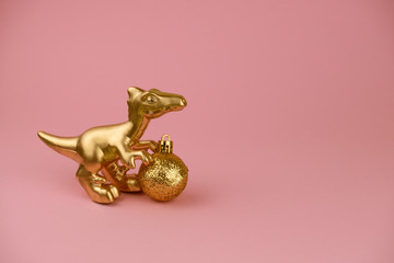 golden dinosaur toy with golden christmas ball on a pastel pink background, trendy modern christmas card with copy space
