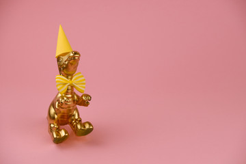 golden dinosaur in a perty hat and bowtie on a pink background with copy space