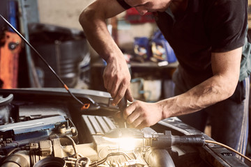 Cropped hands of unrecognizable mechanic doing car service and maintenance. Close up. Repairman...