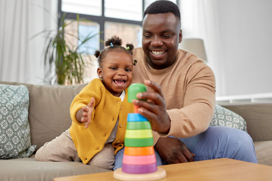 family, parenthood and people concept - happy african american father and baby daughter playing with toy blocks at home