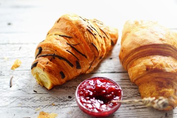 Sweet breakfast. Croissant with raspberries. Raspberry jam in a silver spoon and a bowl. Fragrant pastries on a white wooden background.